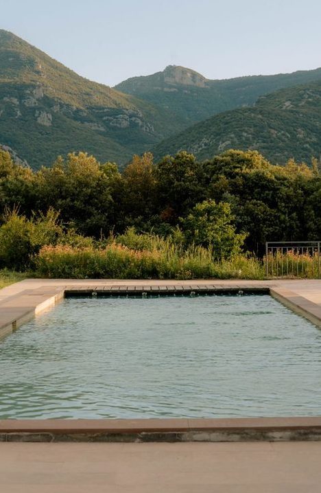 A still outdoor pool with wooded hills behind it